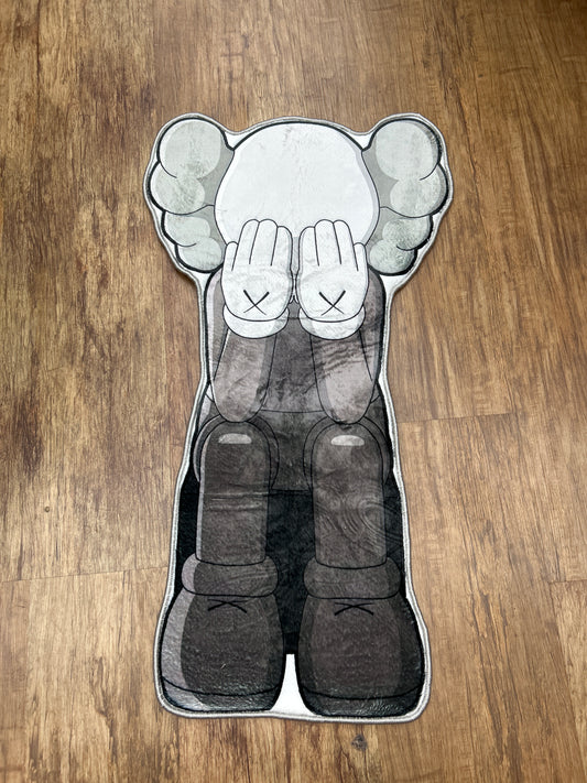 Kaws sitting down covering face rug
